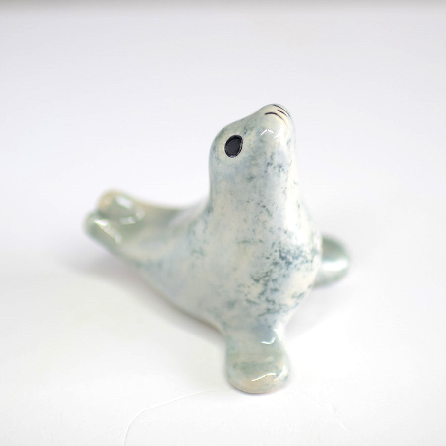 A small ceramic light grey seal in a classic curly pose