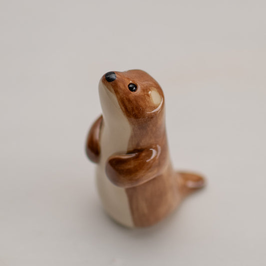 Small ceramic stoat figurine with brown and cream coloring, standing upright and looking upwards
