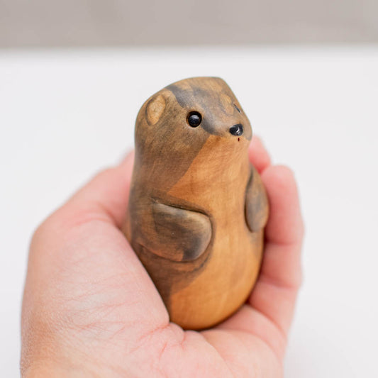 A small ceramic stoat sculpture against a grey backdrop in a hand