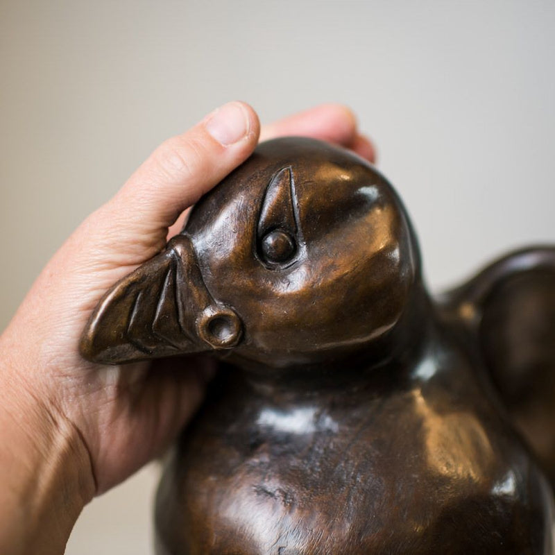 A hand rubbing a bronze Puffin sculpture