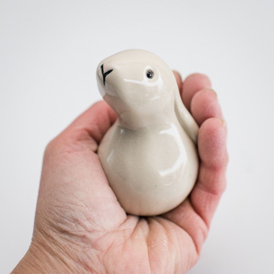 White ceramic bunny being held in a hand against a white background