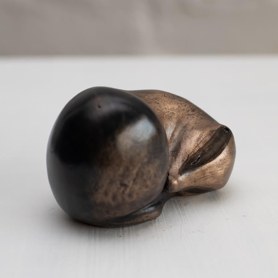 Small bronze sculpture of a badger curled up asleep against a white background