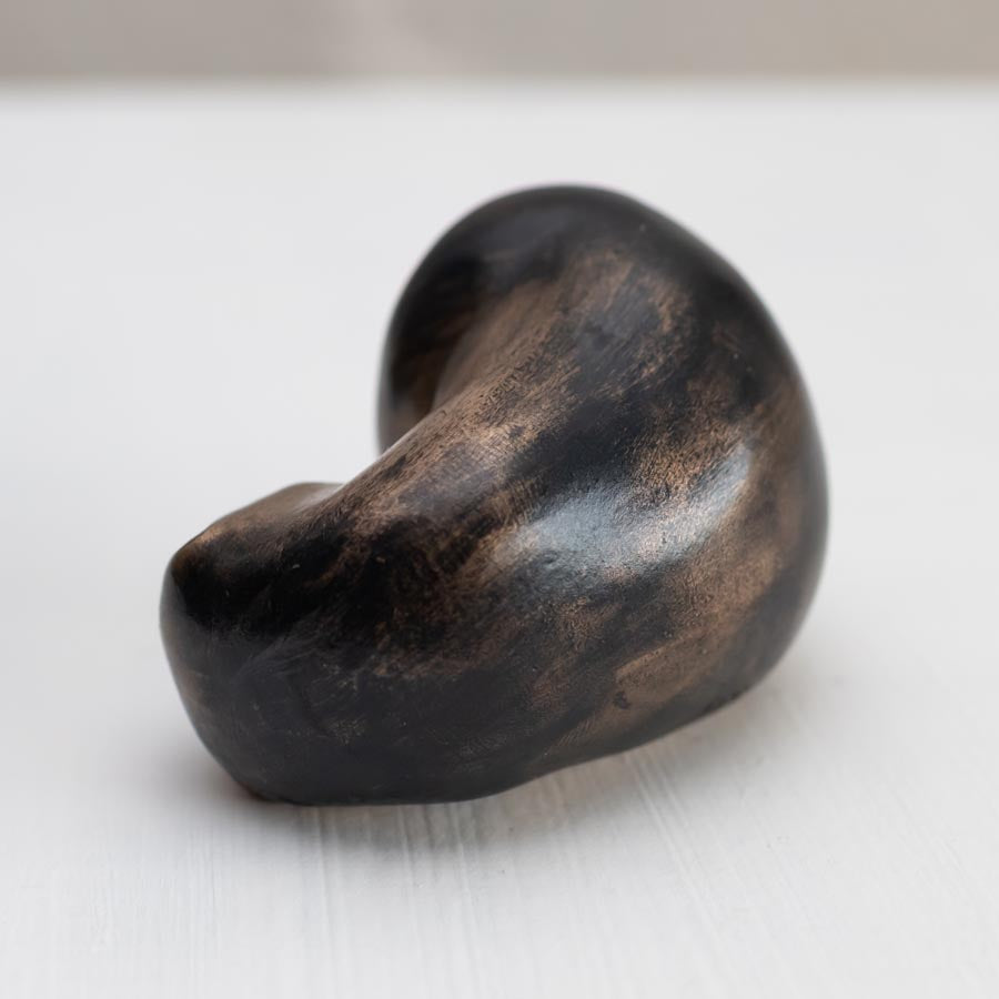Small bronze sculpture of a badger curled up asleep against a white background - rear view