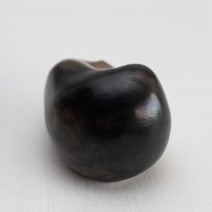 Small bronze sculpture of a badger curled up asleep against a white background - rear view