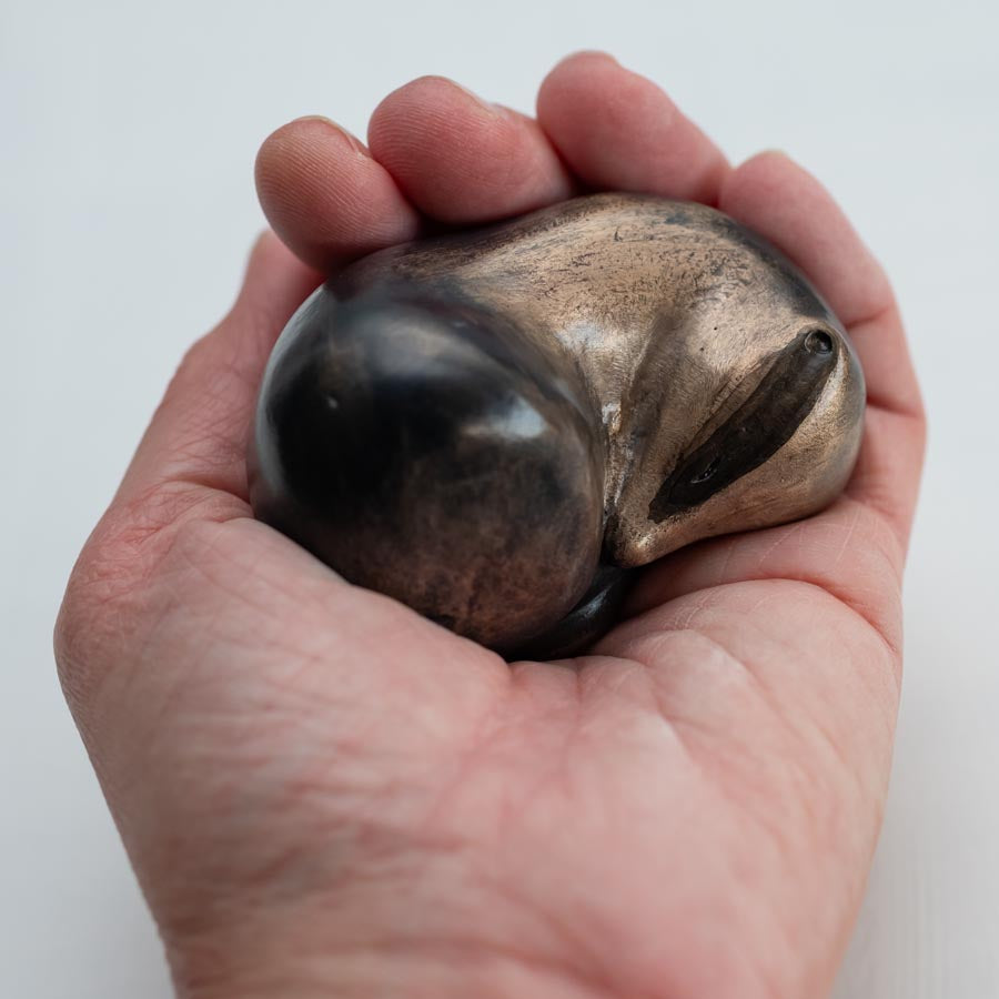 Small bronze sculpture of a badger curled up asleep in a hand against a white background