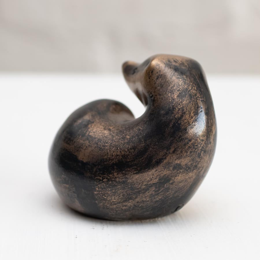 A small bronze badger sculpture against a white background - back view