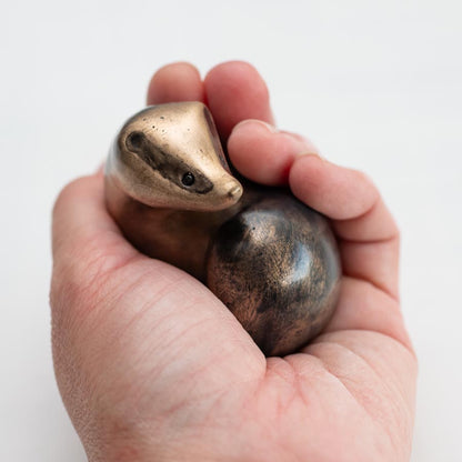 A small bronze badger sculpture in a hand against a white background