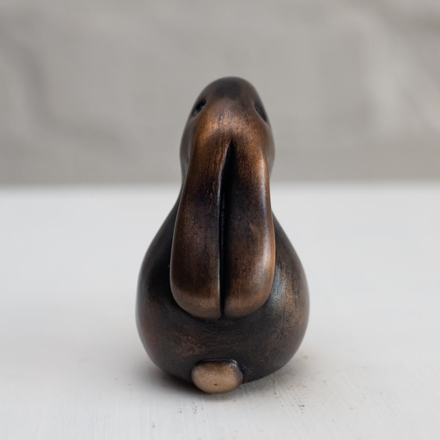 Brown bunny rabbit sculpture in bronze against a white background - rear view