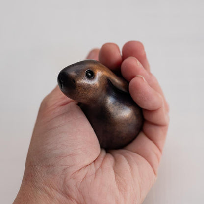 Brown bunny rabbit sculpture in bronze inside a hand against a white background