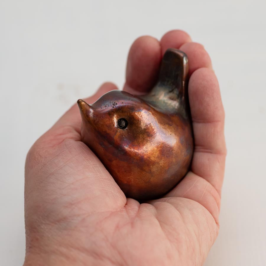hand holding a small bronze wren sculpture against a white background