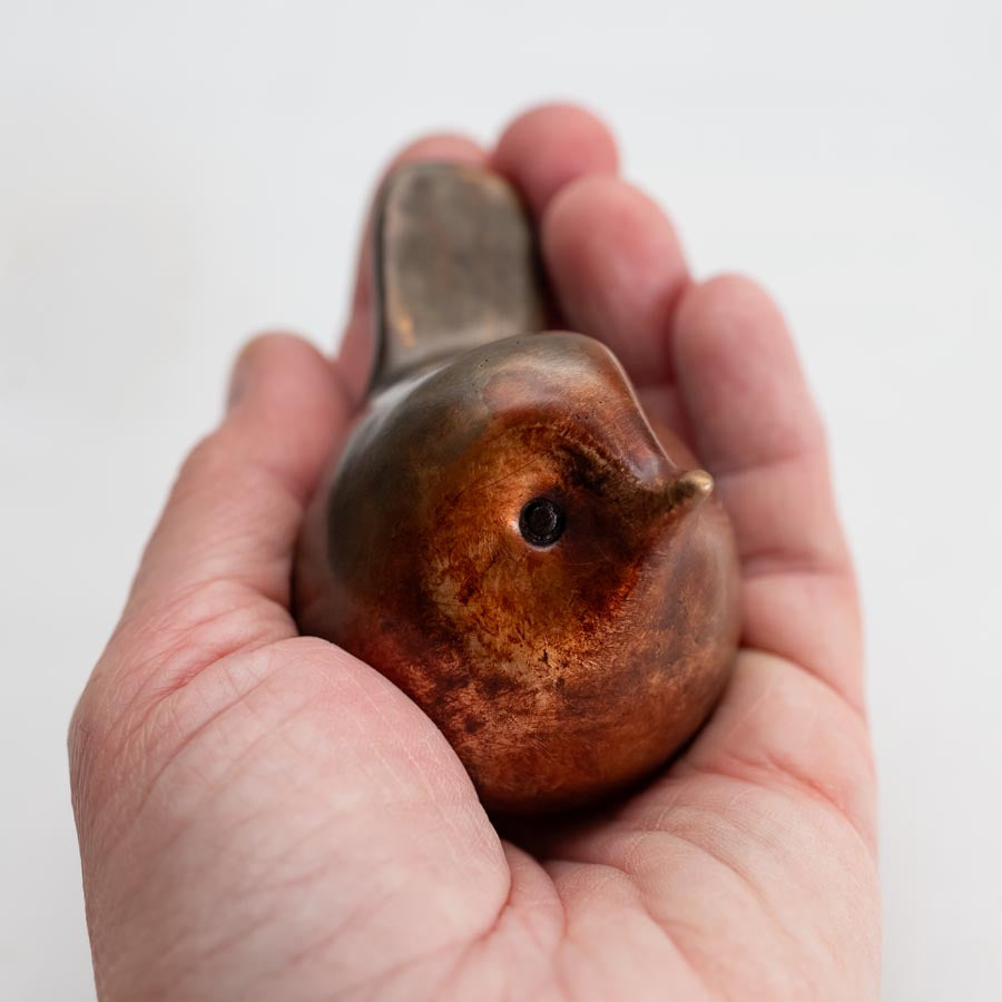 Small bronze Robin sculpture in a hand against a white background