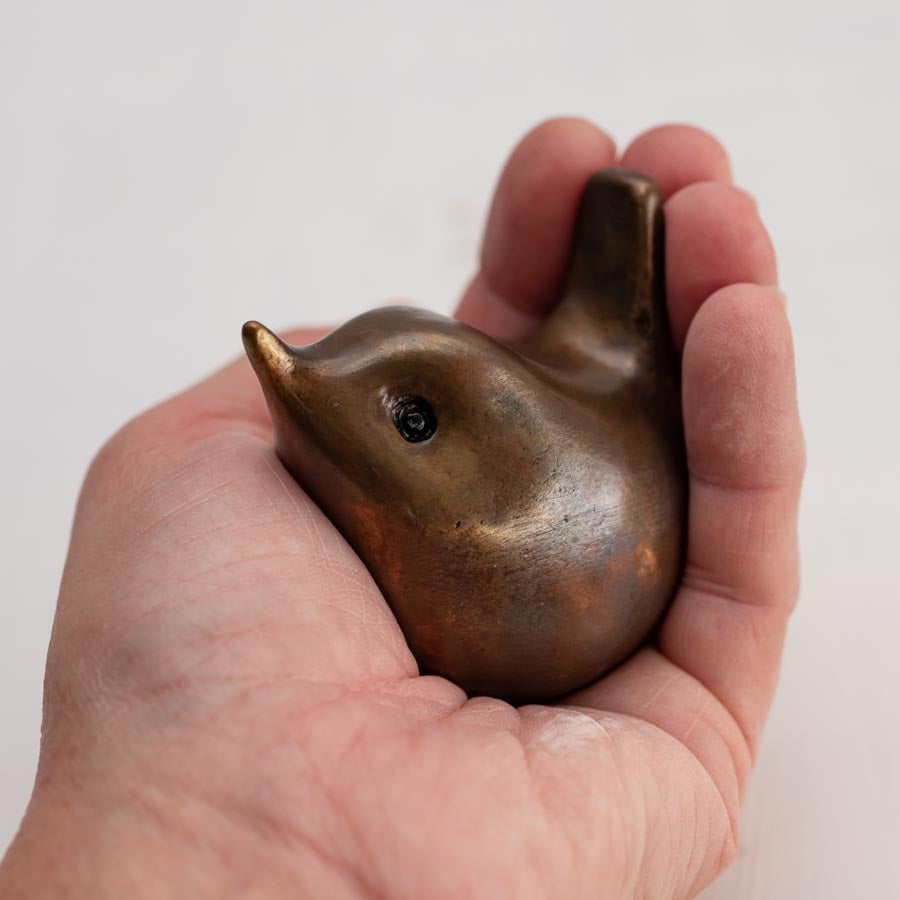 Small bronze wren sculpture in a hand against a white background