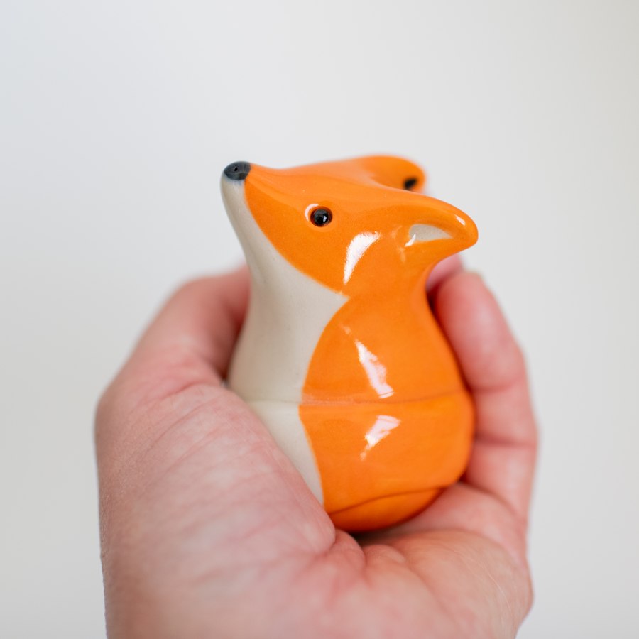 Hand holding a small fox-shaped object against a plain background