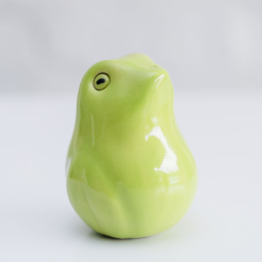 A glossy ceramic frog sculpture in a light lime green color, photographed against a neutral light gray background.