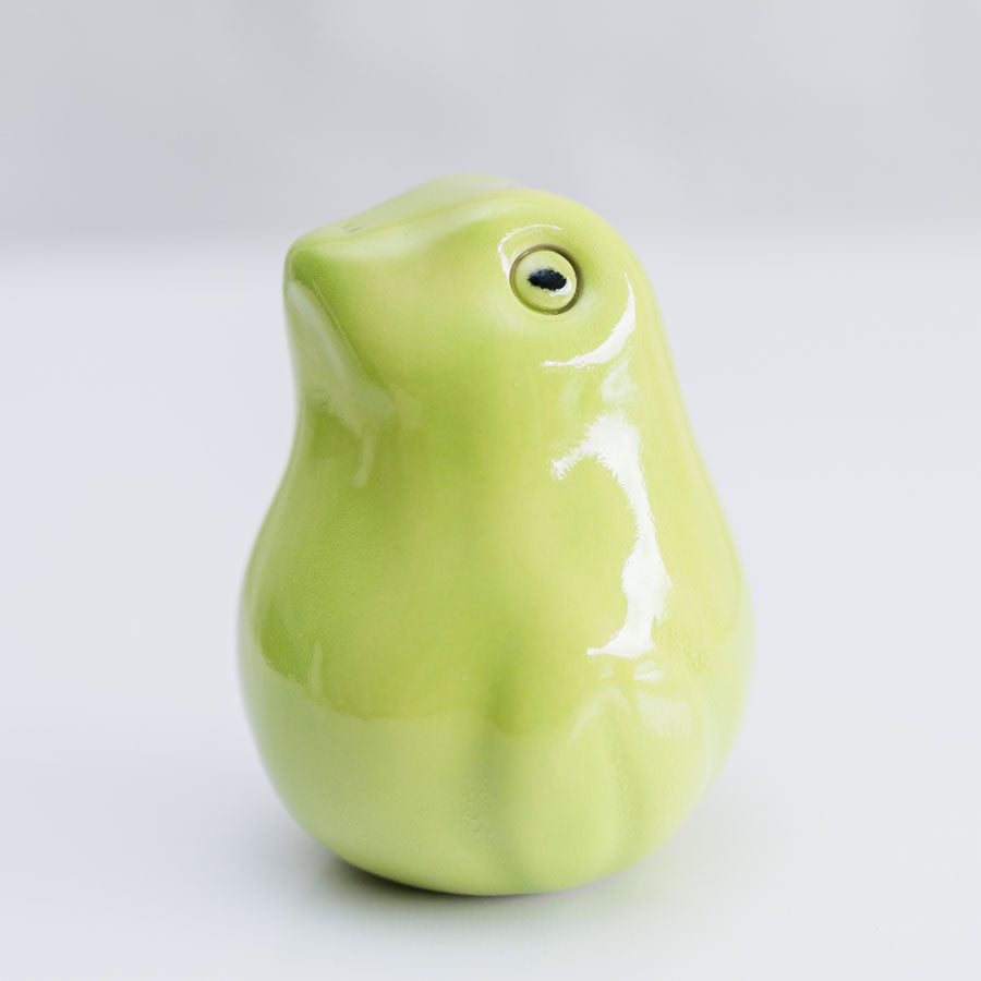 A glossy ceramic frog sculpture in a light lime green color, photographed against a neutral light gray background.