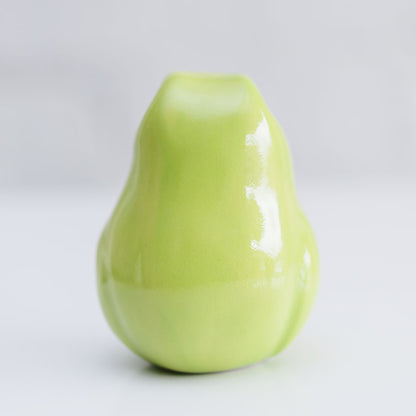 A glossy ceramic frog sculpture in a light lime green color, photographed against a neutral light gray background.