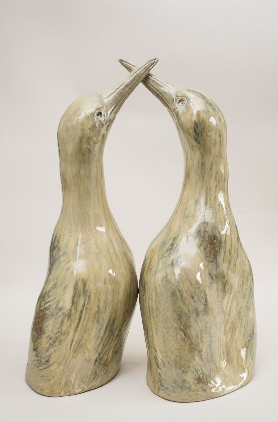 Two ceramic bird sculptures with long necks and beaks touching, light green and brown glaze