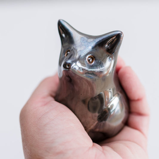 A small metallic fox figurine with a polished silver finish, held in a person's hand against a plain light background.