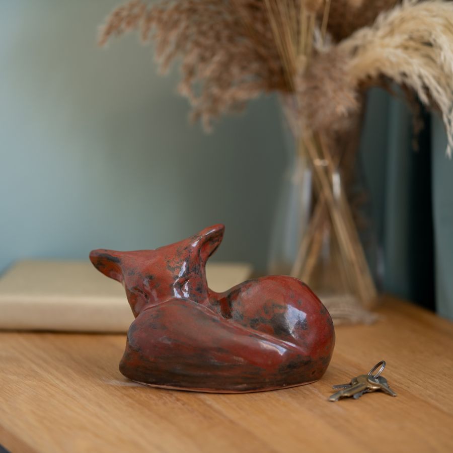 Medium Ceramic Fox Sculpture in red and black, curled up on a wooden surface next to a set of keys