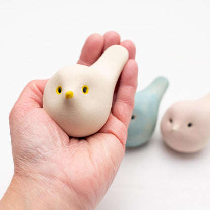 Hand holding a white Spring Pastel Ceramic Joyful Bird, with blue and pink birds in background