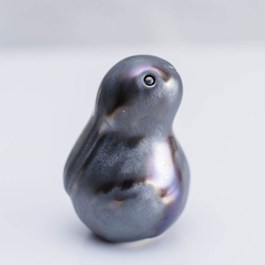 A small sculptural bunny figurine with a glossy, pearlescent dark gray to black finish and subtle iridescent hints, photographed on a clean light gray background.
