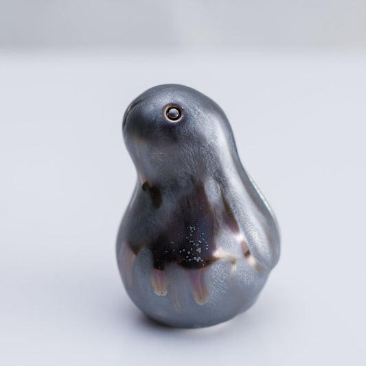 A small sculptural bunny figurine with a glossy, pearlescent dark gray to black finish and subtle iridescent hints, photographed on a clean light gray background.