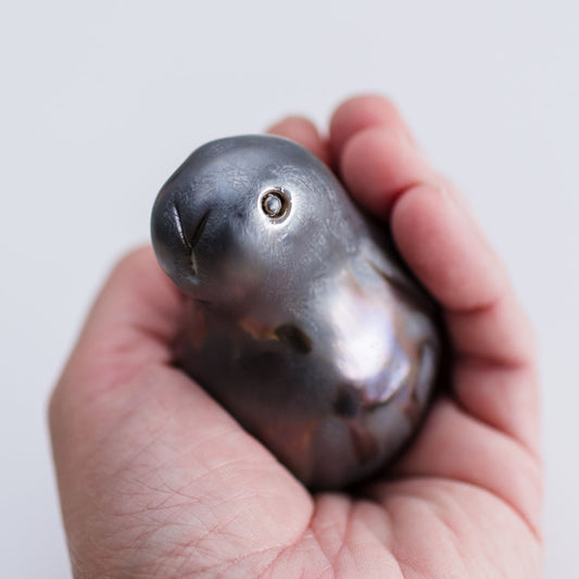 A small sculptural bunny figurine with a glossy, pearlescent dark gray to black finish and subtle iridescent hints, photographed on a clean light gray background in a persons hand
