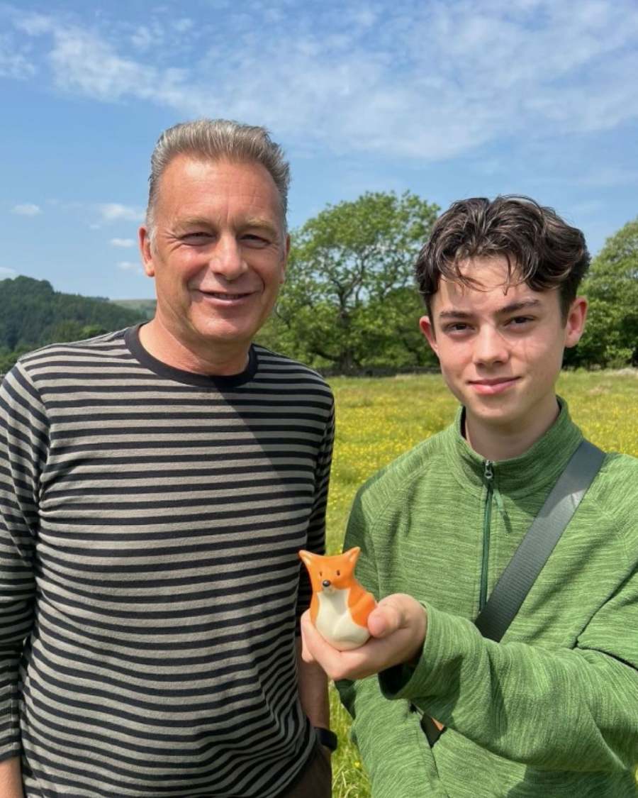 Man in striped shirt and boy in green jacket holding a small fox figurine in a field