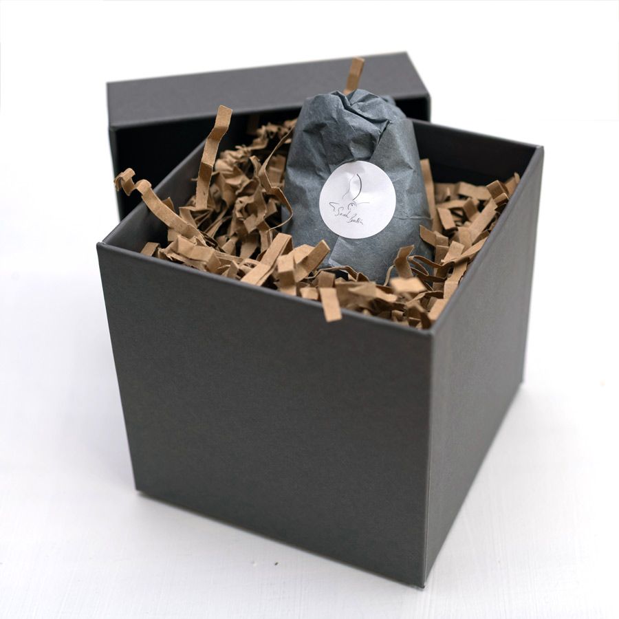 Grey gift box with crinkle paper inside and a tissue paper wrapped sculpture with a white sticker of my logo on it