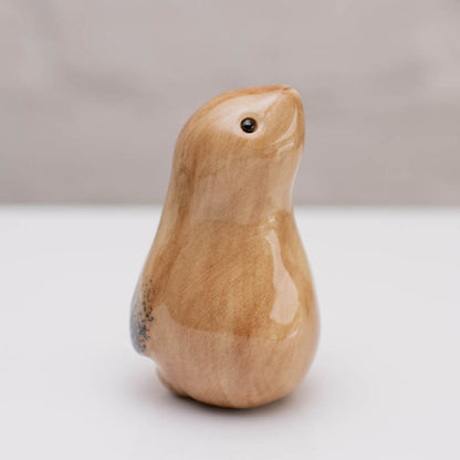 A small glazed ceramic hare figurine in warm tan and light brown tones, standing on a white surface against a soft gray background.