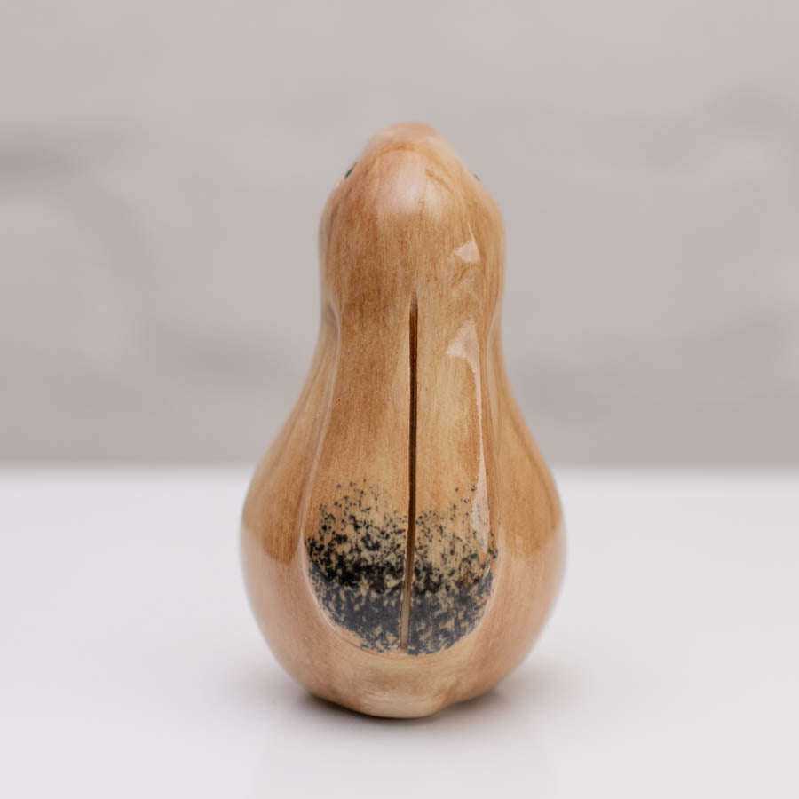 A small glazed ceramic hare figurine in warm tan and light brown tones, standing on a white surface against a soft gray background.