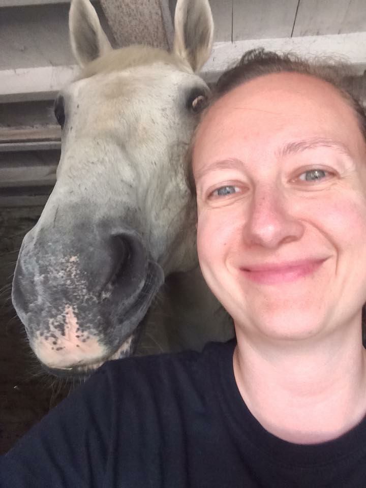Woman in black shirt smiling next to a white horse
