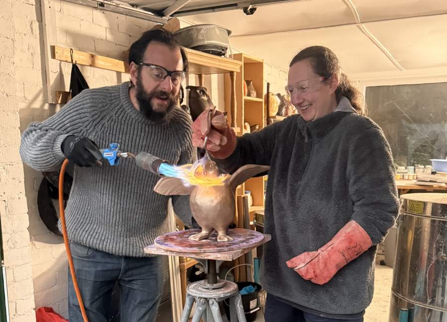 Two people applying heat to a ceramic sculpture of a bird with a torch and tongs