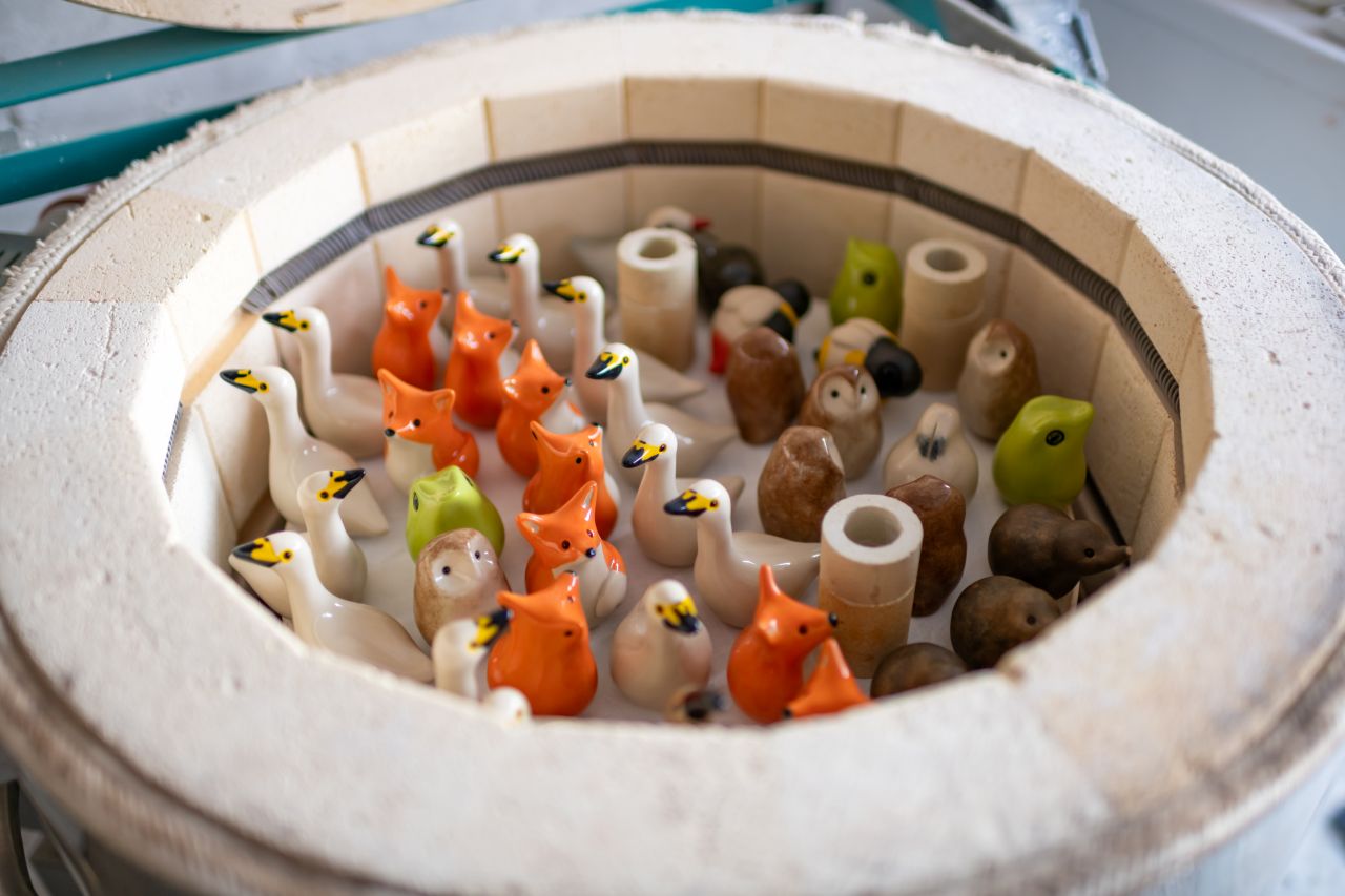 Ceramic kiln filled with small, unglazed animal figurines including swans, foxes, owls, and hedgehogs