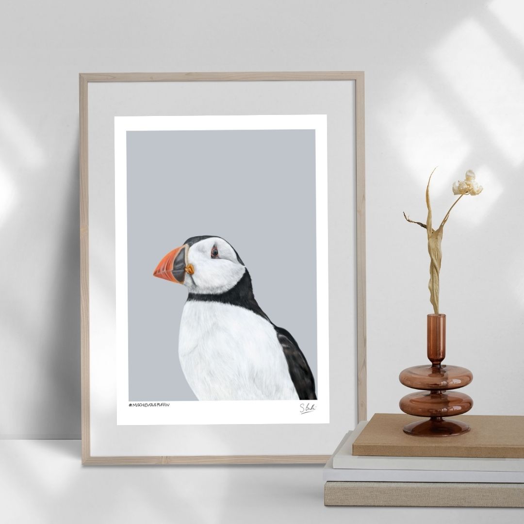 A Puffin artwork in a frame on a table with books and a vase