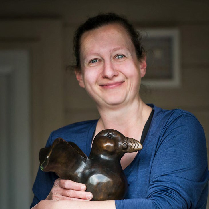 Woman in blue shirt holding a bronze bird sculpture