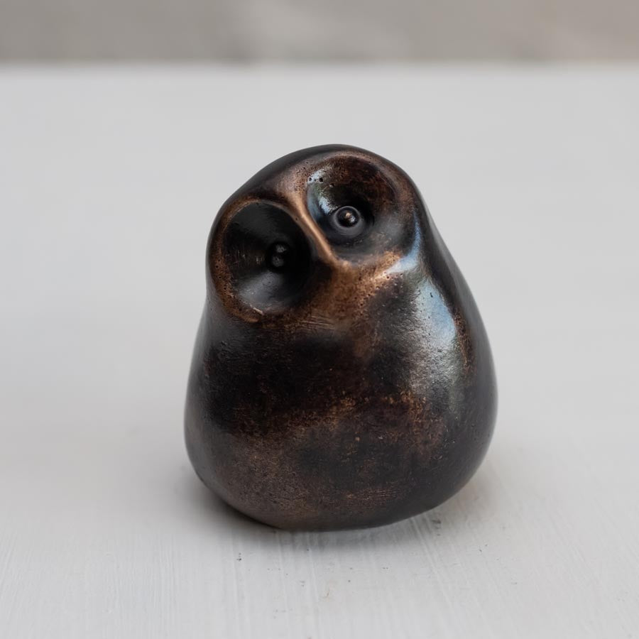 Small smooth bronze owl sculpture on a plain background
