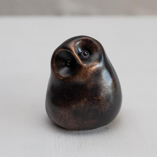 Small smooth bronze owl sculpture on a plain background