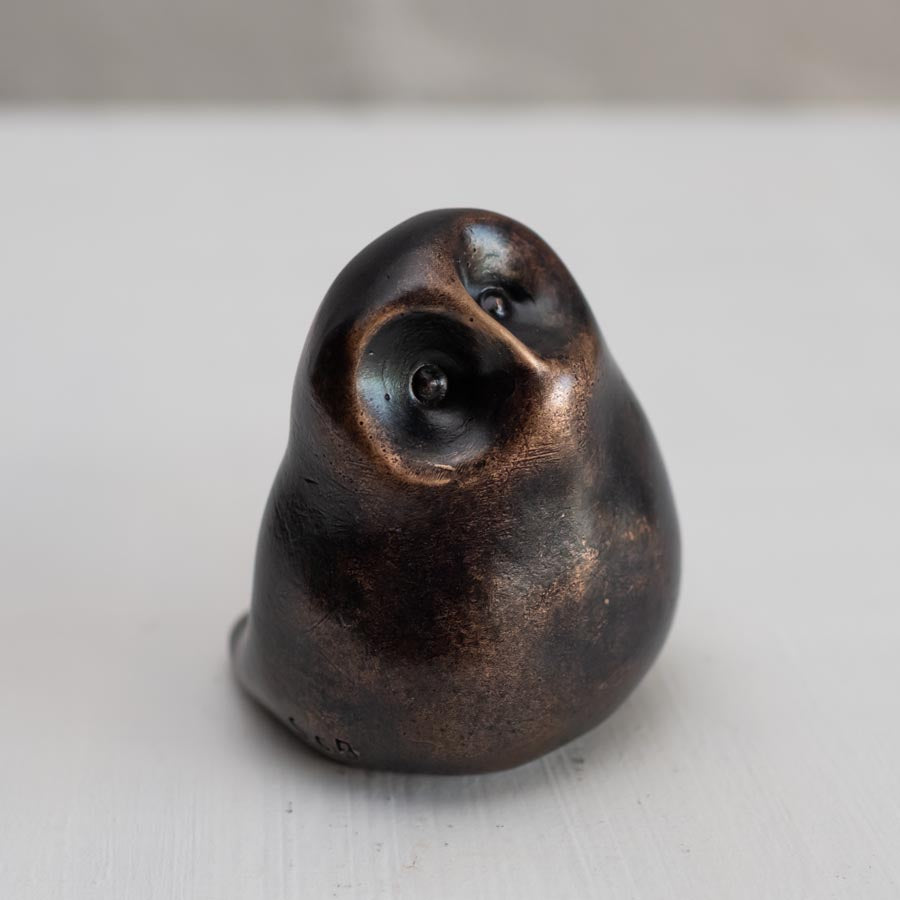 Small smooth bronze owl sculpture on a plain background