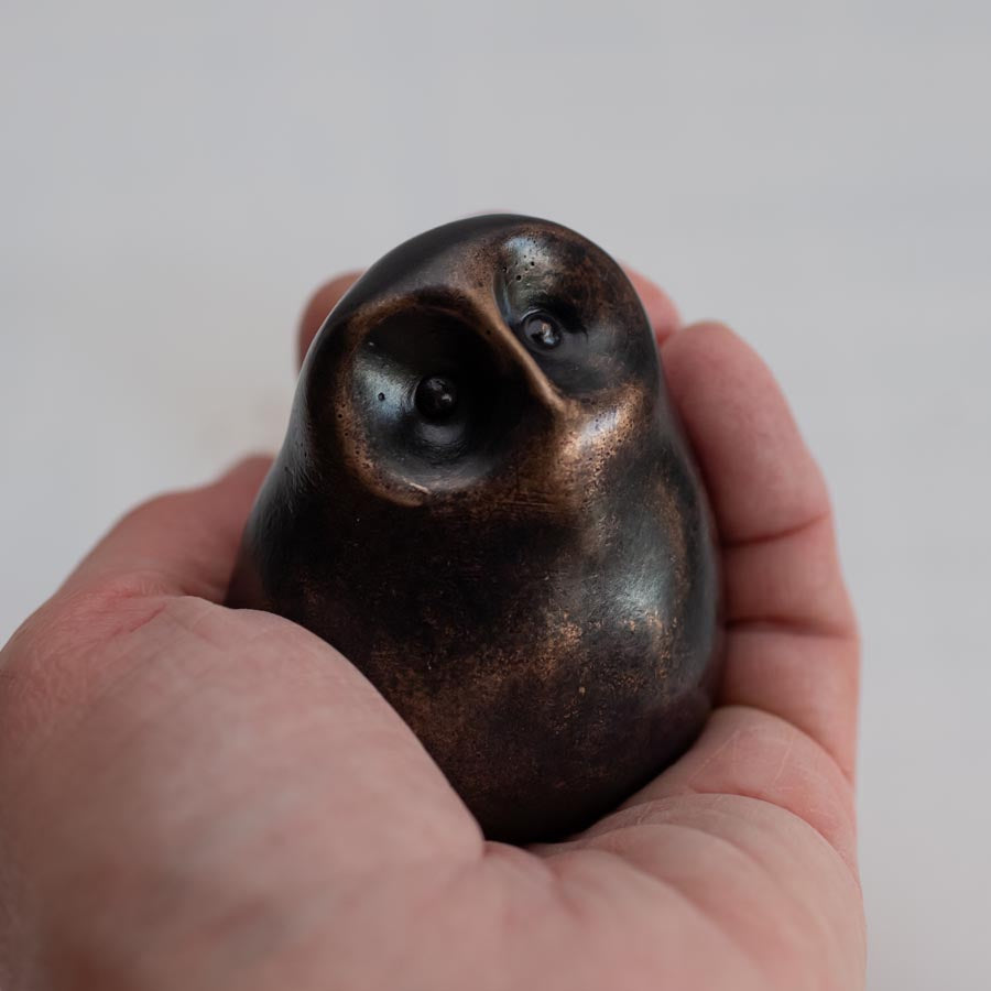 Small smooth bronze owl sculpture in a hand against a plain background