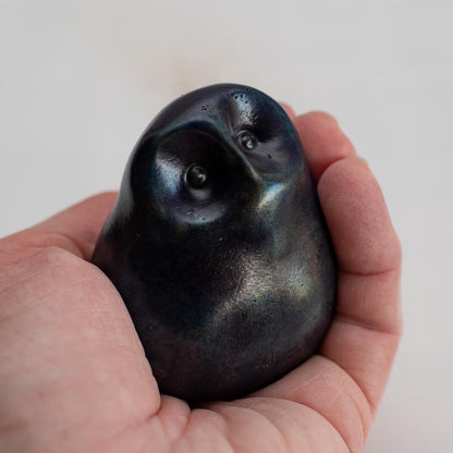 Deep blue small bronze owl sculpture in a hand on a white background