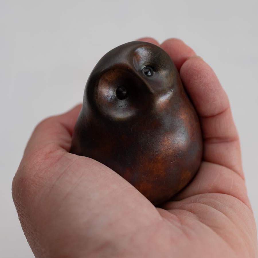hand holding a Brown coloured bronze owl sculpture against a white background