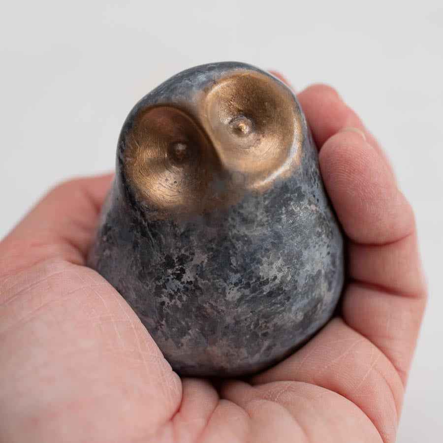 A hand holding a mall grey coloured bronze owl sculpture against a white background