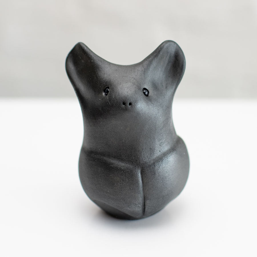 A matte black ceramic bat figurine standing upright on a white surface against a light gray background.