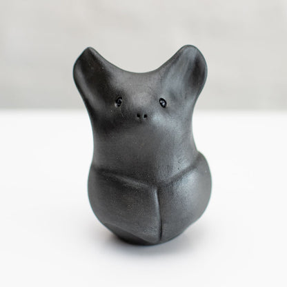 A matte black ceramic bat figurine standing upright on a white surface against a light gray background.