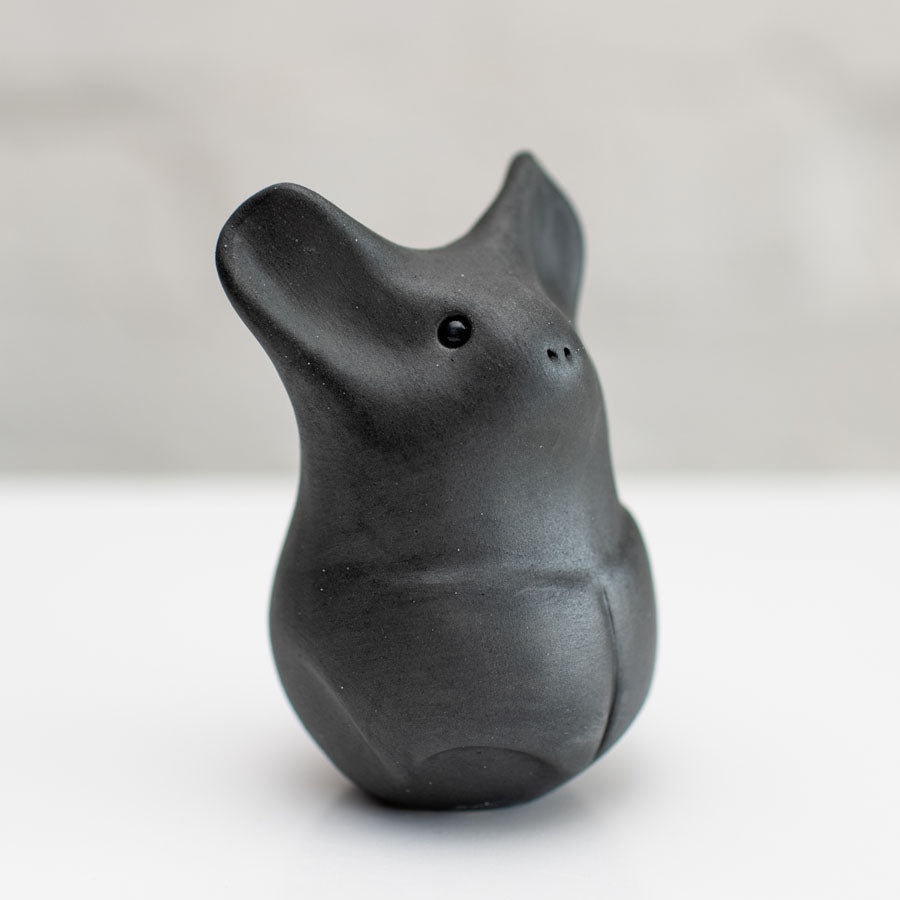 A matte black ceramic bat figurine standing upright on a white surface against a light gray background.