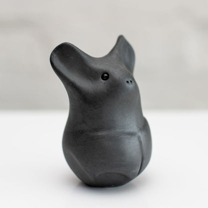 A matte black ceramic bat figurine standing upright on a white surface against a light gray background.
