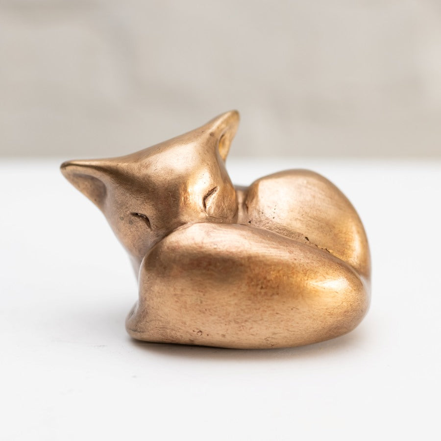 Sleepy Bronze Fox Sculpture curled up on a white surface