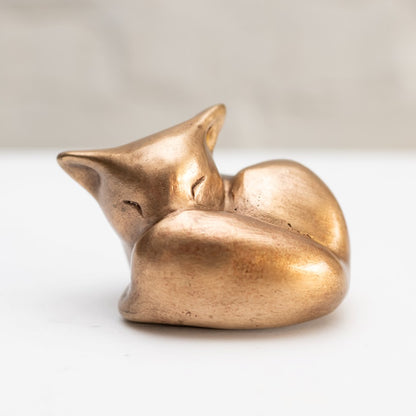 Sleepy Bronze Fox Sculpture curled up on a white surface