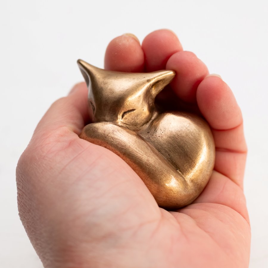 Bronze fox figurine held in a hand against a white background